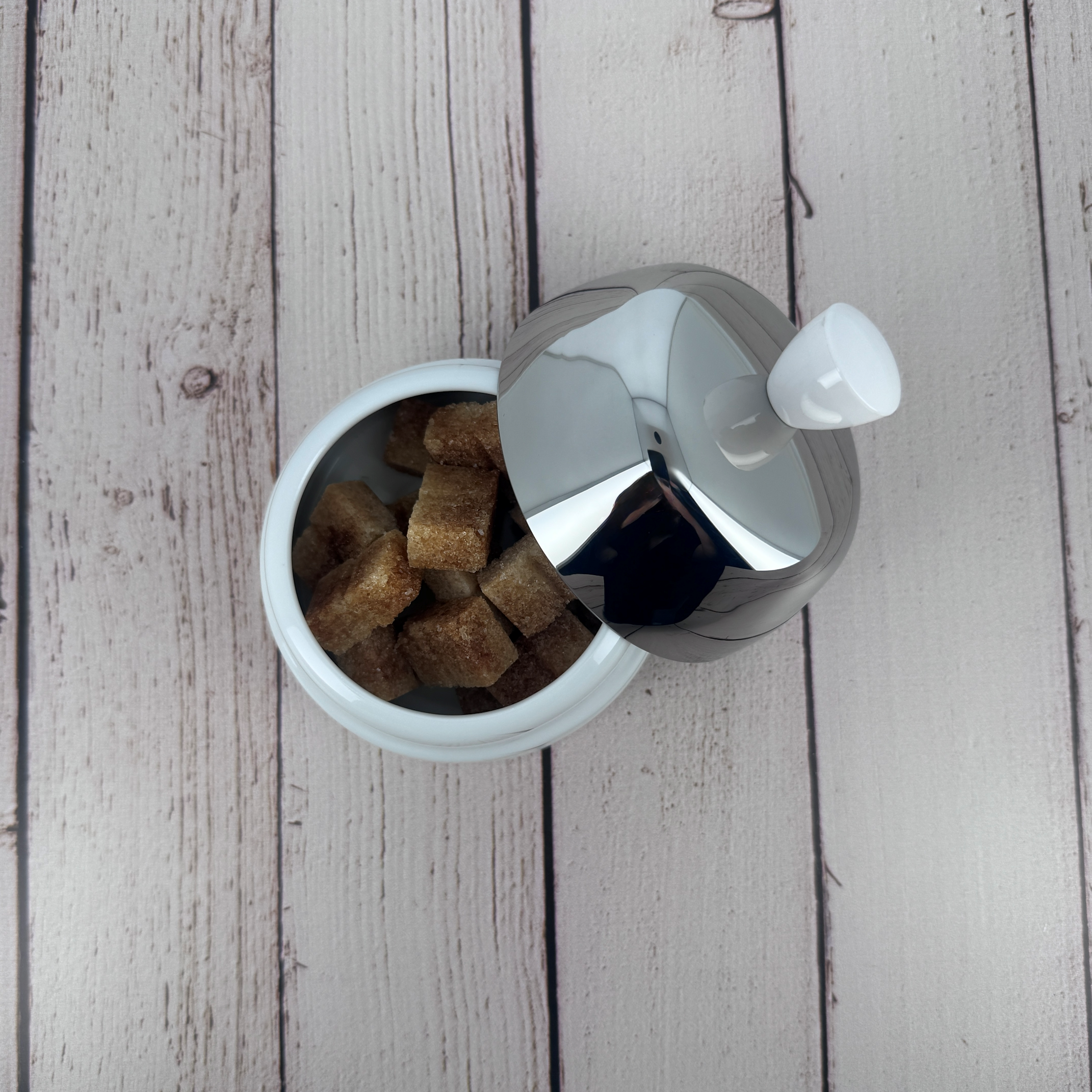 Discover the Salam white porcelain sugar bowl by Degrenne, paired with a mirror-polished steel lid, filled with cane sugar cubes.