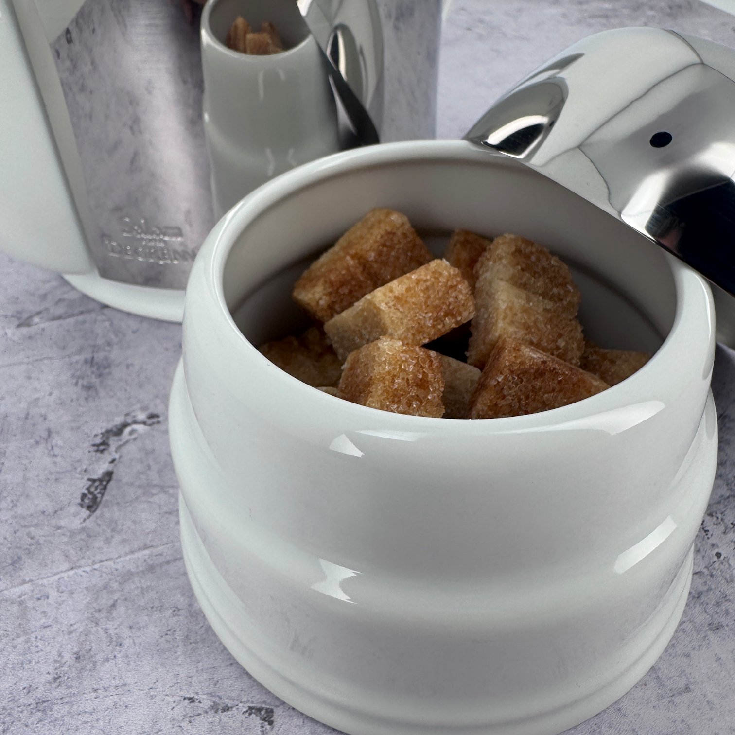 Close-up of the Salam white porcelain sugar bowl by Degrenne, generously filled with cane sugar cubes, styled with matching tableware.